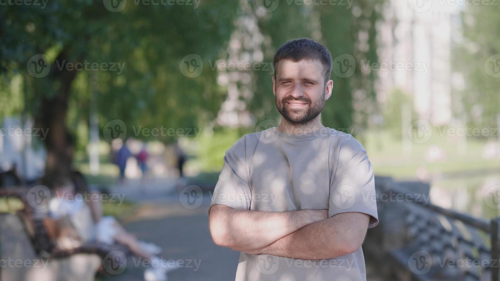 A cheerful man joyfully poses by the shimmering water with sunlight gently filtering through the lush trees photo