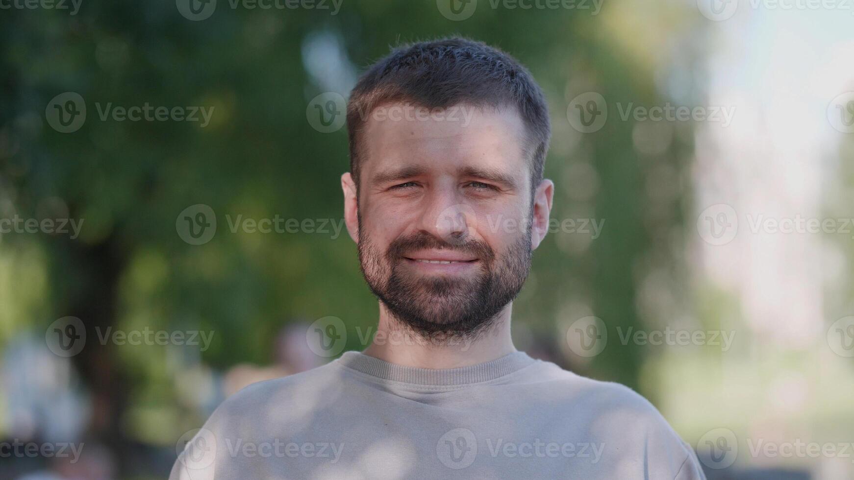 A cheerful man stands in the park, surrounded by lush greenery, radiating positivity, warmth, and friendliness photo