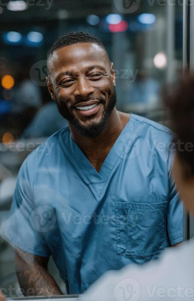 Smiling doctor wearing blue scrubs talking to patient behind glass in hospital photo