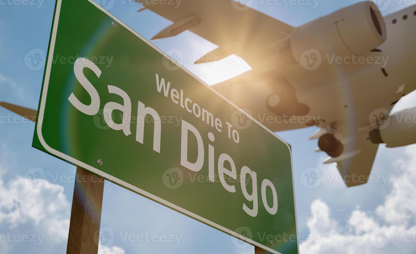 Welcome To San Diego Green Road Sign Against a Blue Sky and Clouds with Low Flying Airplane Above. photo