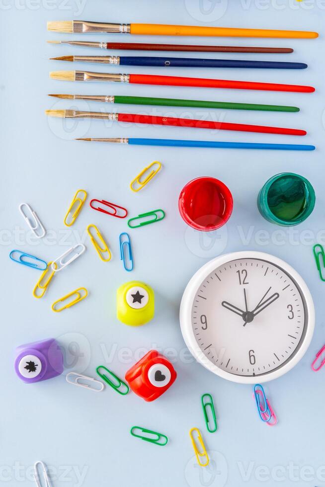 Creative back to school supplies flatlay with colorful markers paint brushes toy bus clock clips paper punches and vivid paperclips symbolizing learning routine education and artistic expression photo