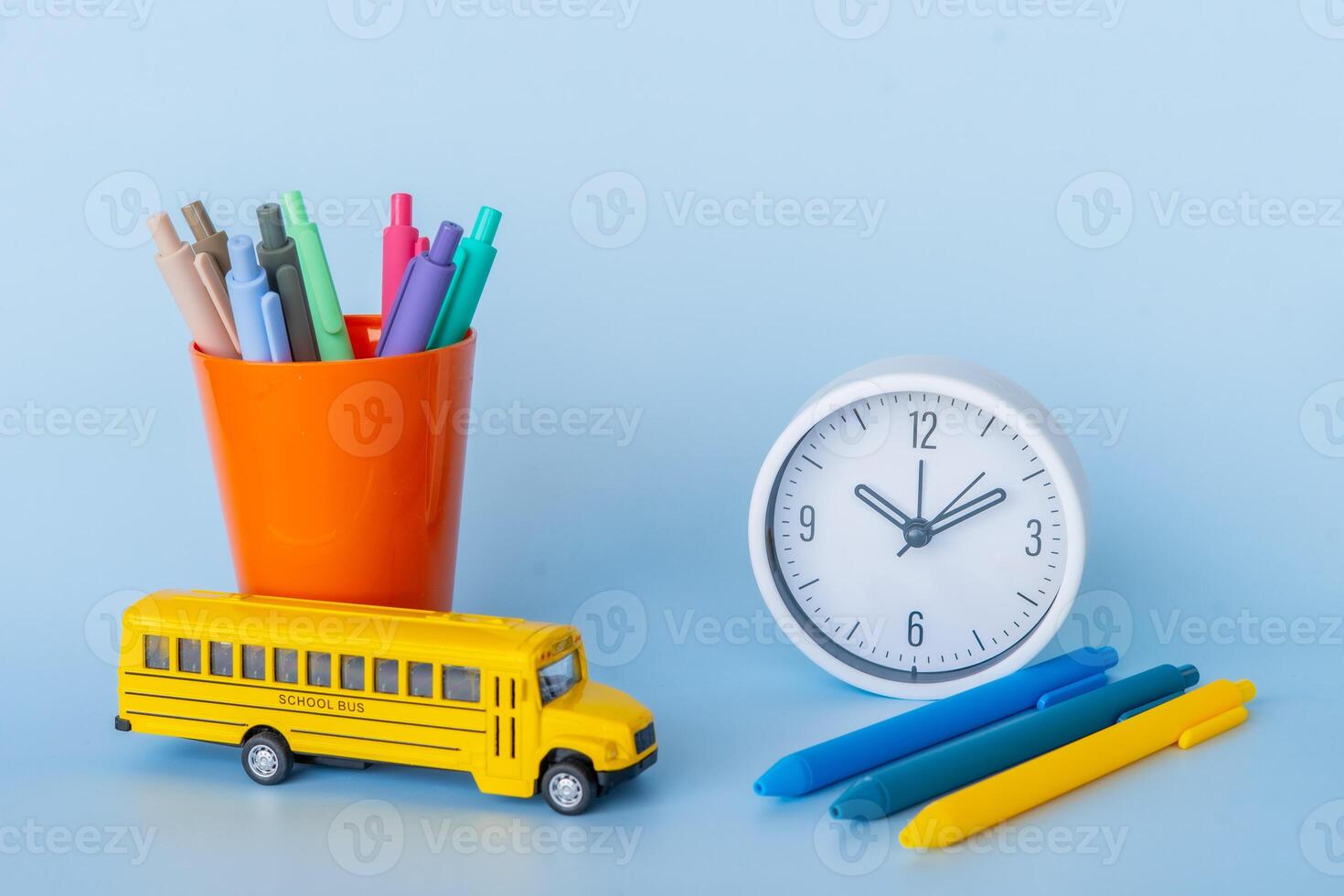 Flat lay with orange cup full of pens clock and toy bus reflecting school start morning routine kids organization bright stationery focus planning academic year and cheerful educational themes photo