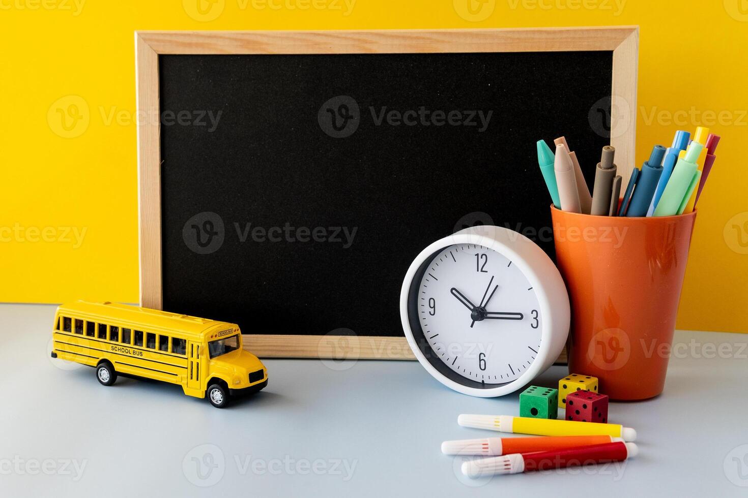 Back to school concept with blackboard colorful markers yellow school bus plastic dice modern clock and bright pens in orange cup vibrant layout symbolizing schedule creativity and school life photo