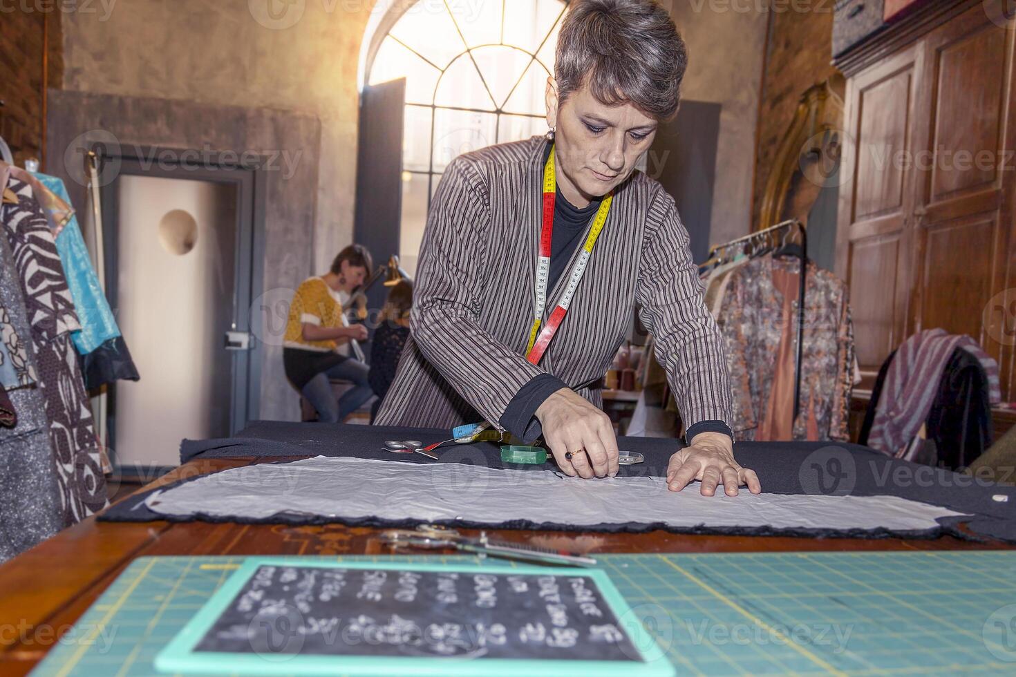 the dressmaker cutting and measuring fabrics for new dresses in her workshop photo