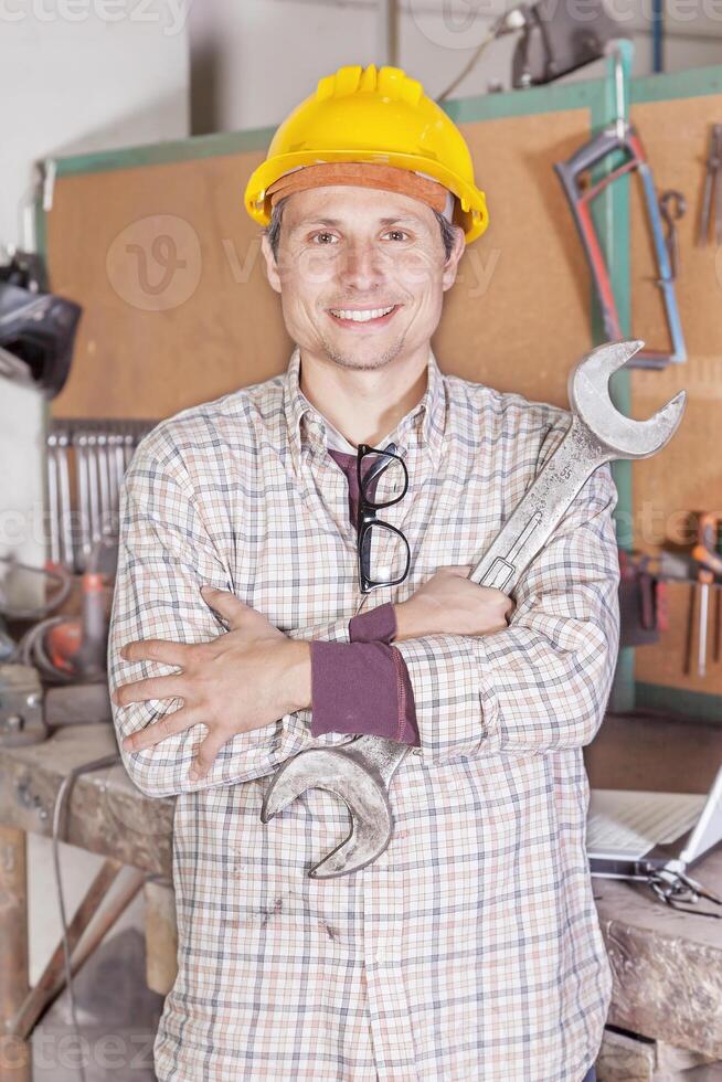 portrait of young metalworker with yellow protective helmet and a wrench photo