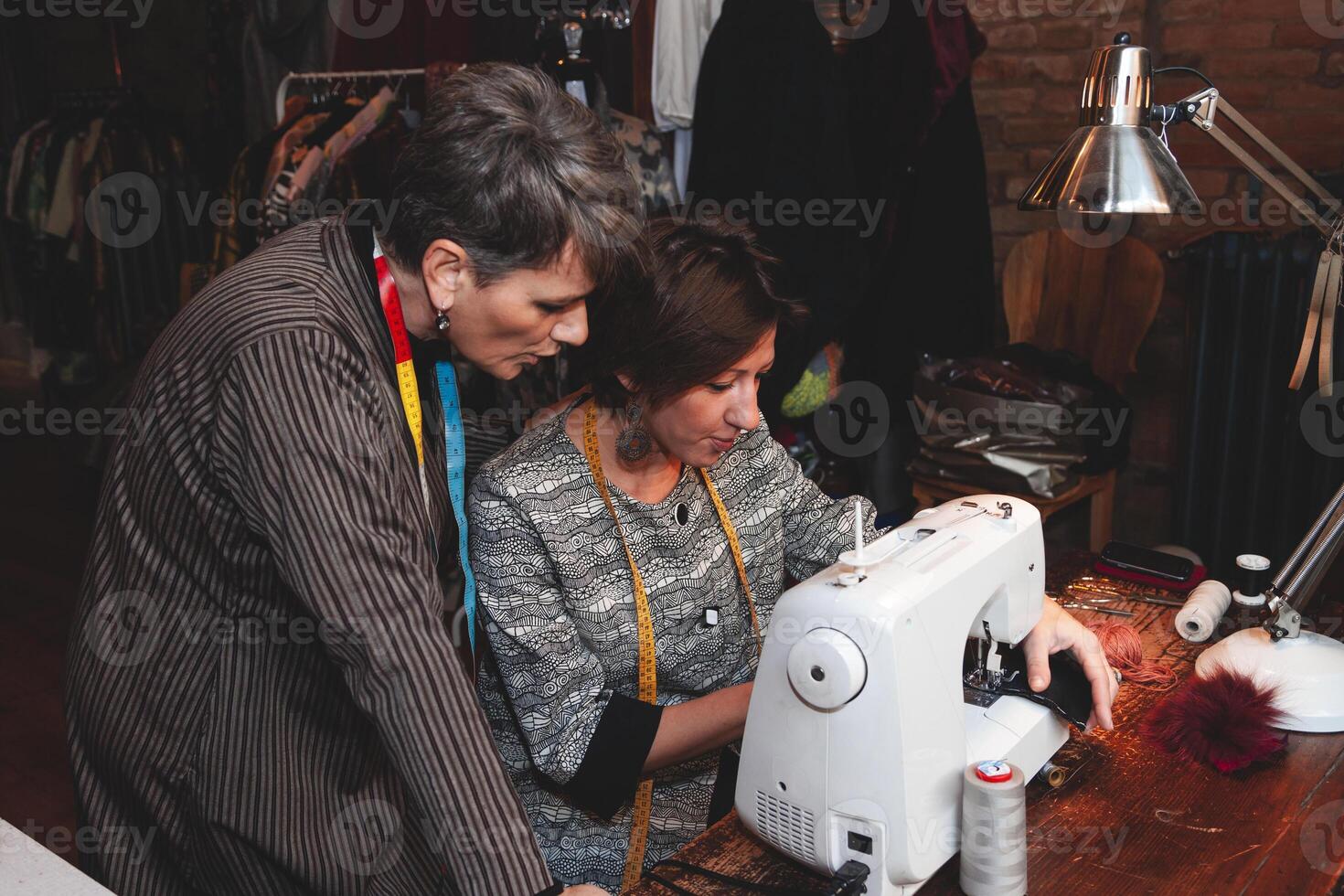 couple of fabric workers sewing a dress with sewing machine in a craft fashion house photo