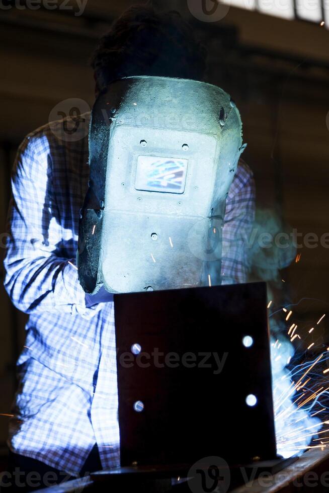 worker welding a metal frame wearing a protective mask in an industrial environment photo