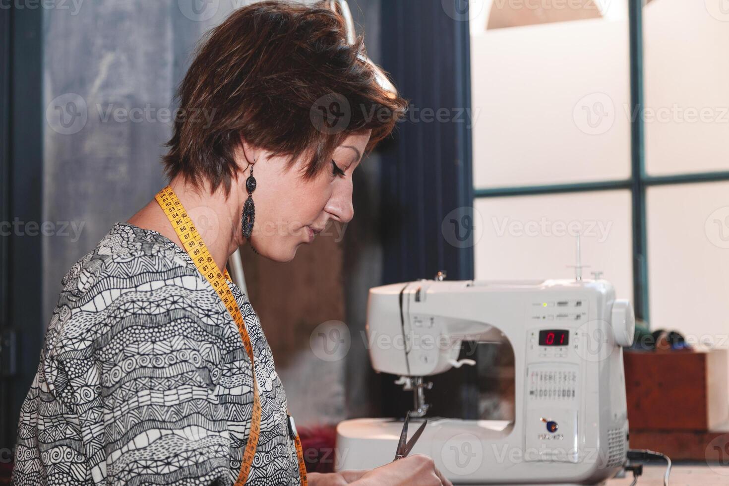 profile portrait of beautiful young seamstress working with white sewing machine photo