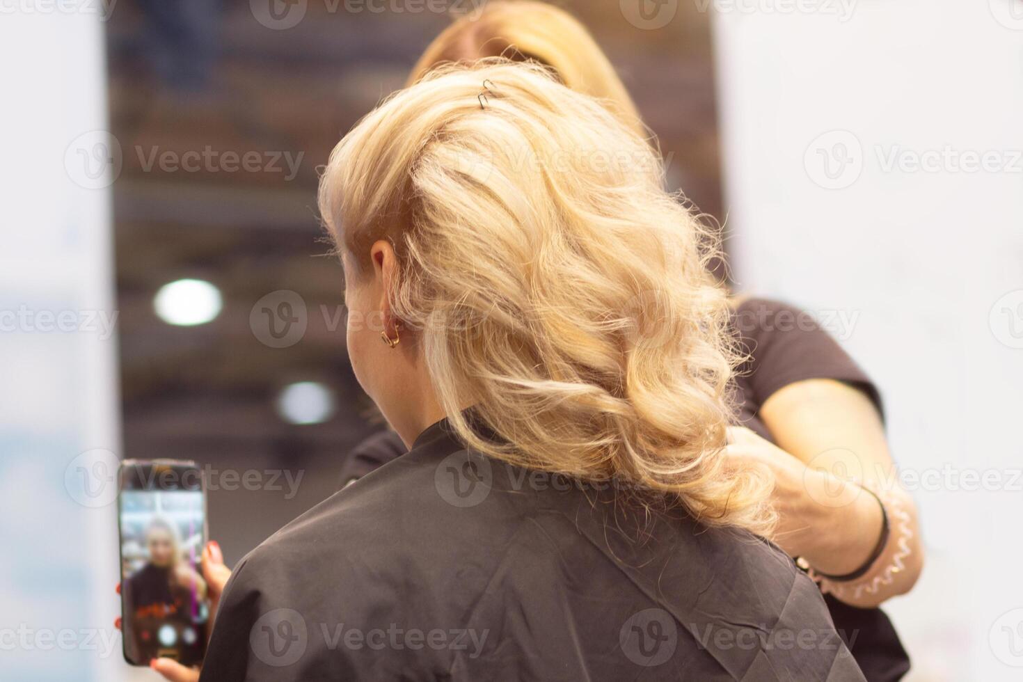 Closeup of hairdresser hands using hairspray styling on woman's healthy golden hair at barber salon photo