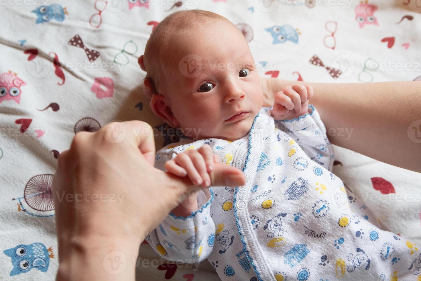 A charming newborn child will be by the hands of his mother lying on the bed photo