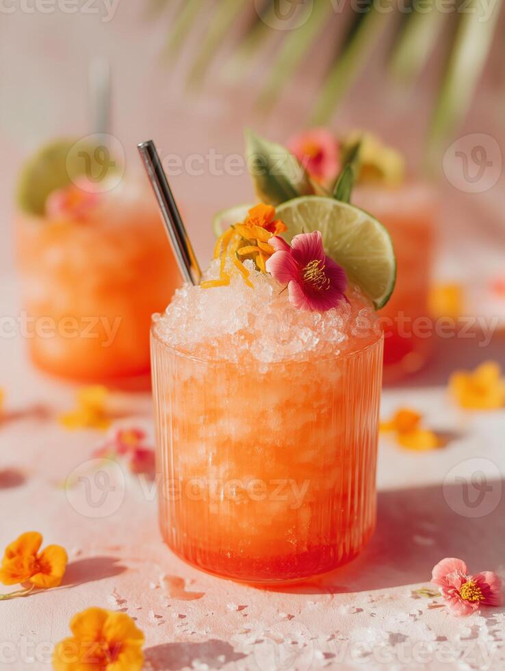 Refreshing summer cocktail in orange-pink tone with crushed ice, lime slice, edible flowers, and a metal straw in a ribbed glass. photo
