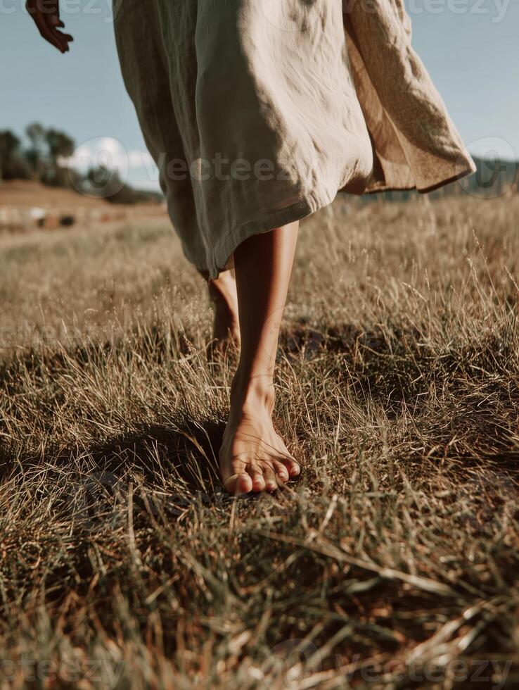 A peaceful and airy photo of a barefoot woman walking through dry golden grass in soft afternoon sunlight.