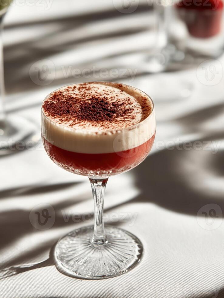Elegant cocktail in a vintage-stemmed glass, featuring two layers a deep ruby-red bottom and a creamy frothy top, dusted with cocoa powder. photo