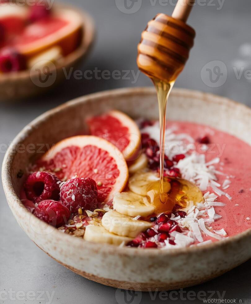 A delicious pink smoothie bowl topped with grapefruit slices, banana, raspberries, shredded coconut, and pomegranate seeds. photo