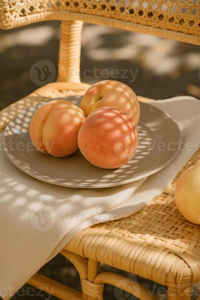 Close-up of ripe white peaches on a ceramic plate placed on a woven rattan chair, soft white textile underneath the plate, intricate shadow pattern cast by sunlight through the wicker backrest photo