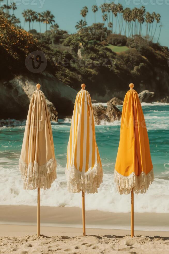 Three closed vintage-style beach umbrellas with fringe details, standing on a sunny tropical beach with turquoise waves in the background and palm trees in the distance. photo