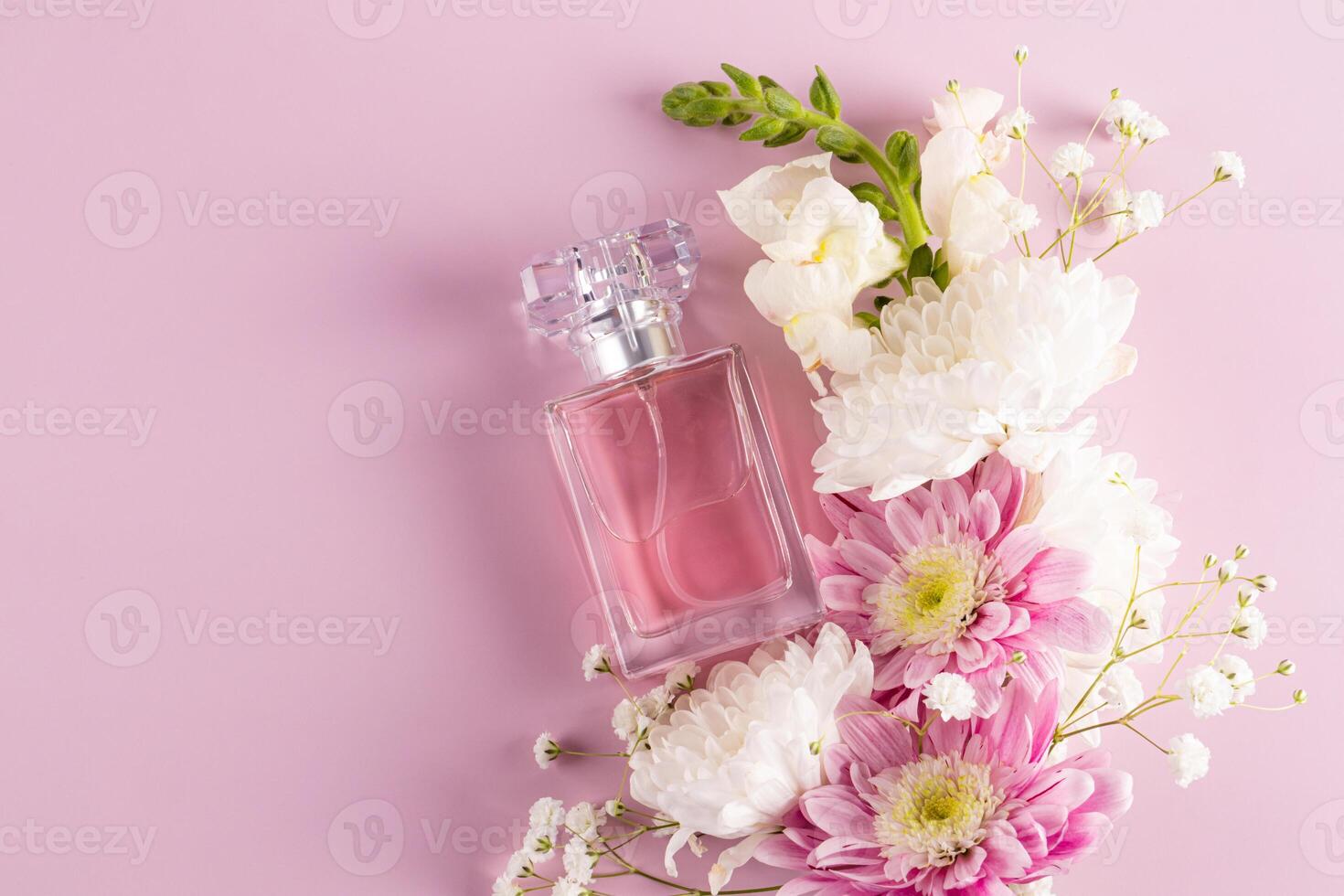 An elegant bottle of perfume with a refined floral scent on a pink background among of white and pink flowers . A blank bottle mockup. top view photo