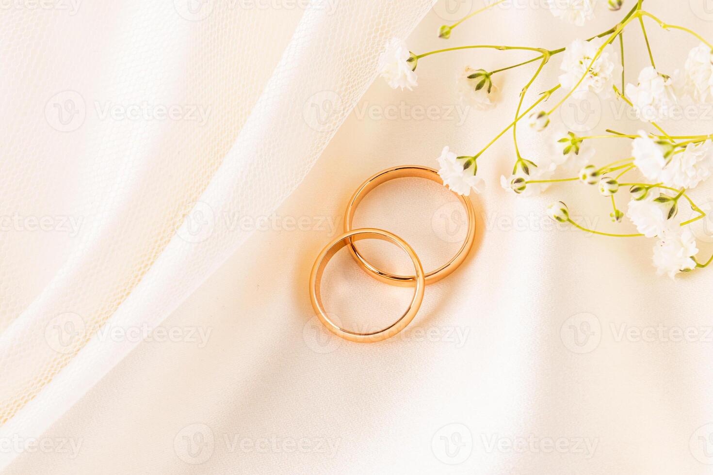 A pair of gold wedding rings, a symbol of love, lie on a chic beige satin fabric between the soft folds fabric. top view. The concept of the wedding photo