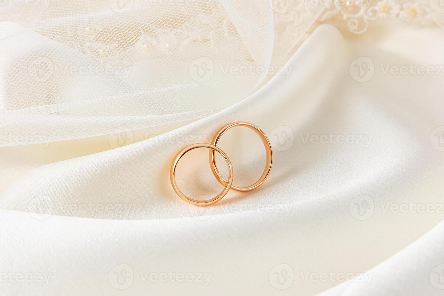 Two gold classic wedding rings leaned on chic folds of cream-colored satin satin. Front view. Wedding invitation layout, postcard. photo