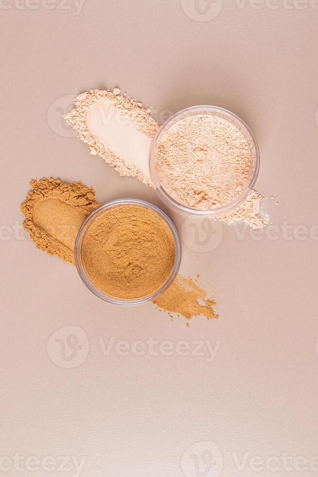 Two cosmetic glass jars with dry loose powder in natural and bronze tones stand on the powder texture samples. vertical top view. A copy space. photo
