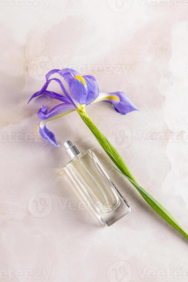 An elegant bottle of perfume or cosmetic spray on light marble background with a chic blue iris flower. The top vertical view . Fragrance presentation photo