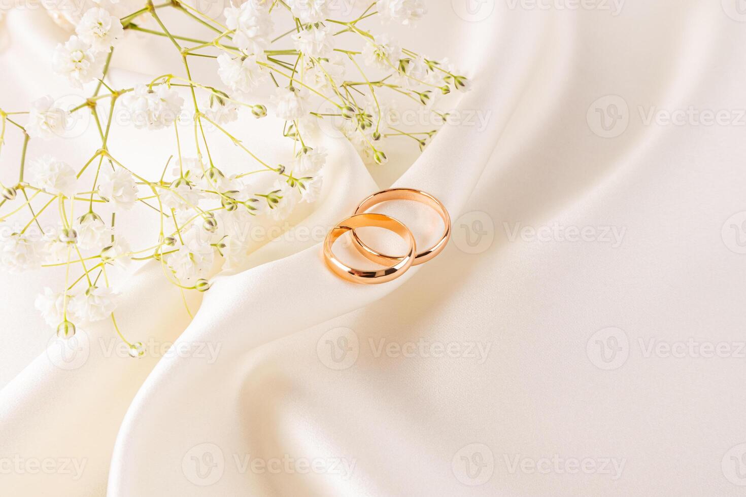 Two gold wedding rings are lying on a beautiful fold of cream-colored satin. Delicate flowers of gypsophila. top view. The concept of the wedding photo