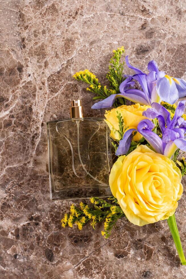 A chic bottle of perfume on a marble brown background with bright yellow and blue flowers. A blank bottle mockup. Fragrance presentation. top view photo