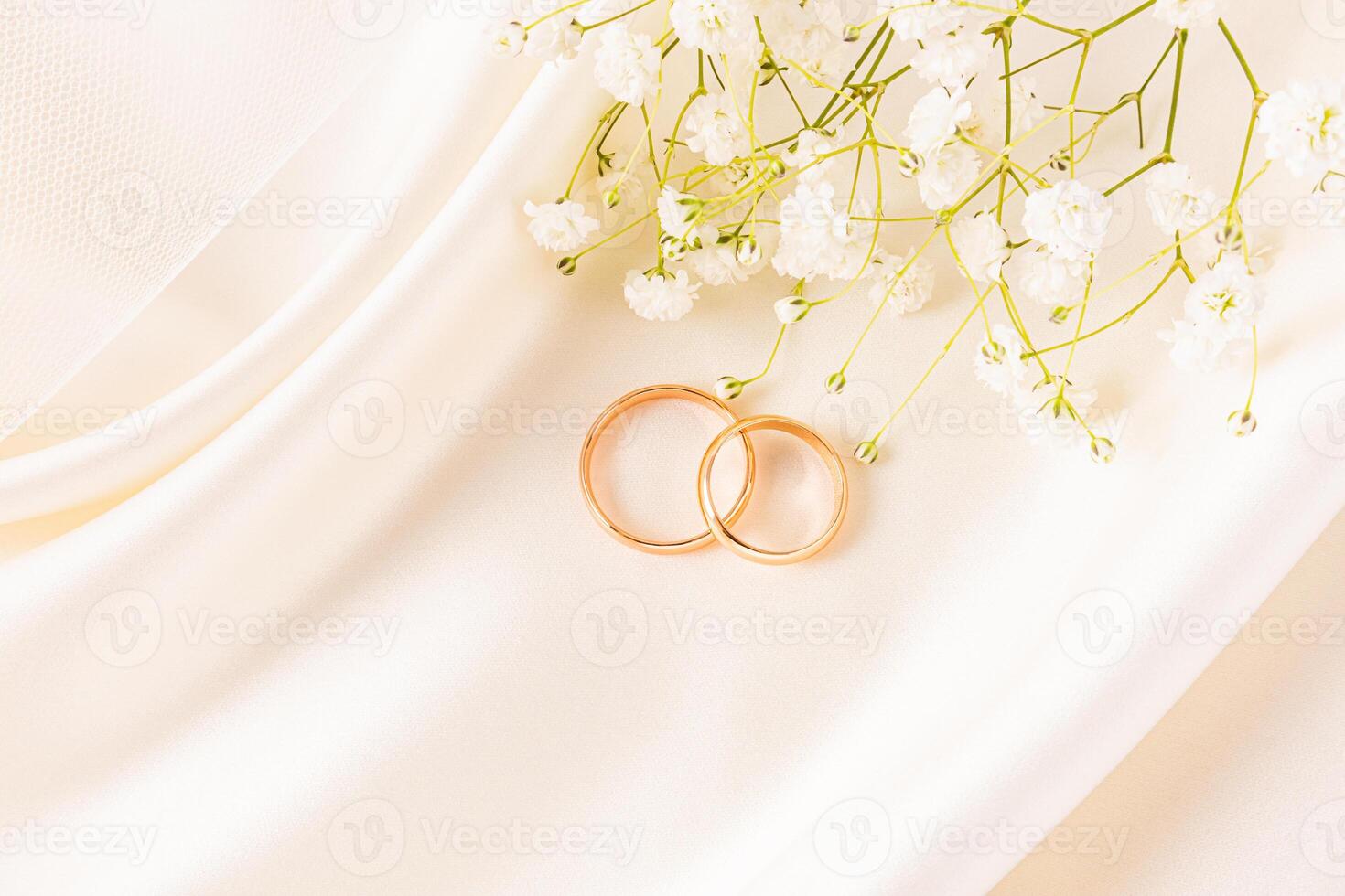 Two gold wedding rings lie on a beautiful satin background of beige tone, with delicate waves of fabric and a sprig of white gypsophila. postcard. photo