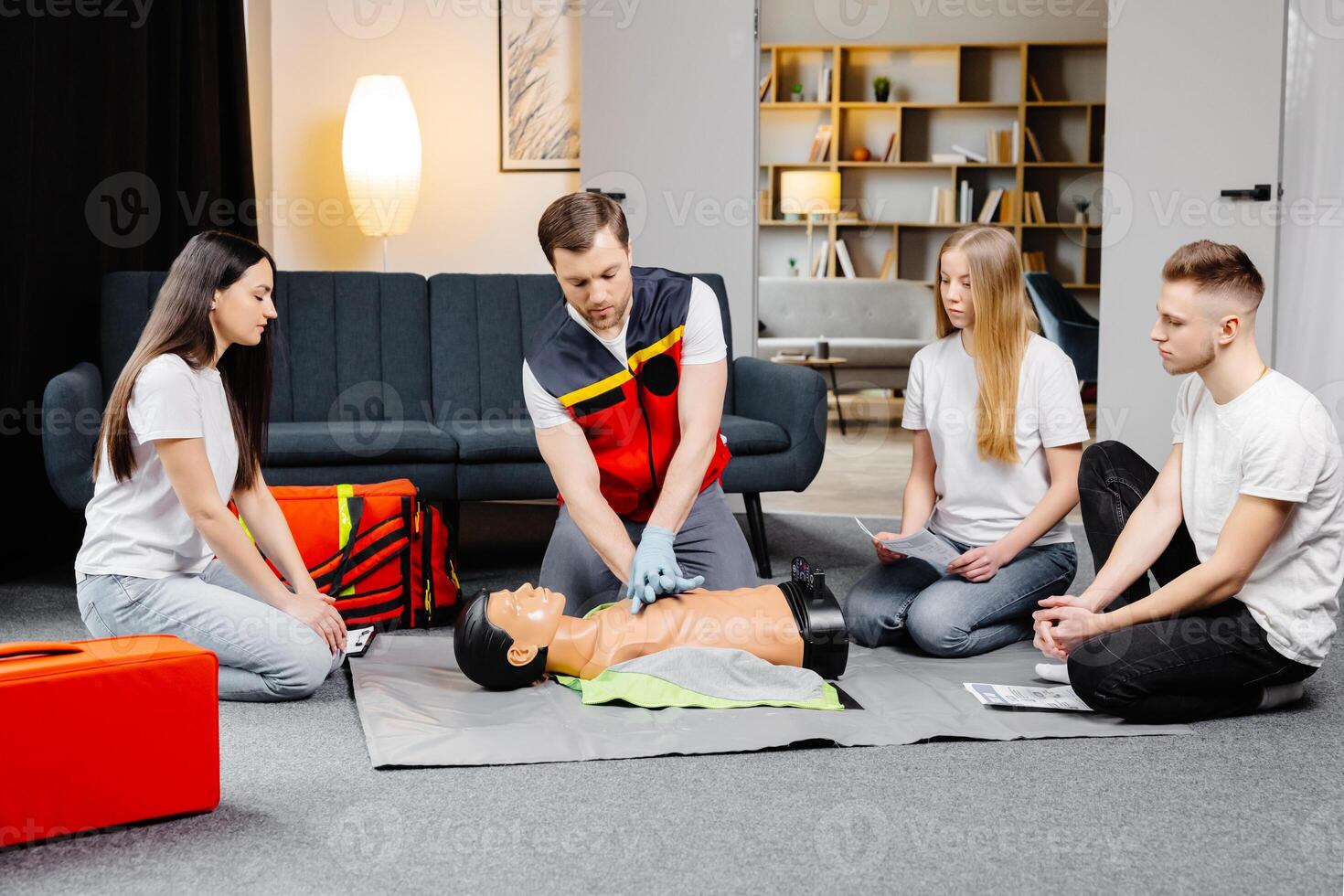 Man instructor helping to make first aid heart compressions with dummy during the group training indoors photo