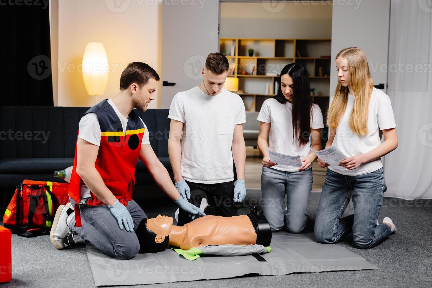 Man instructor helping to make first aid heart compressions with dummy during the group training indoors. photo