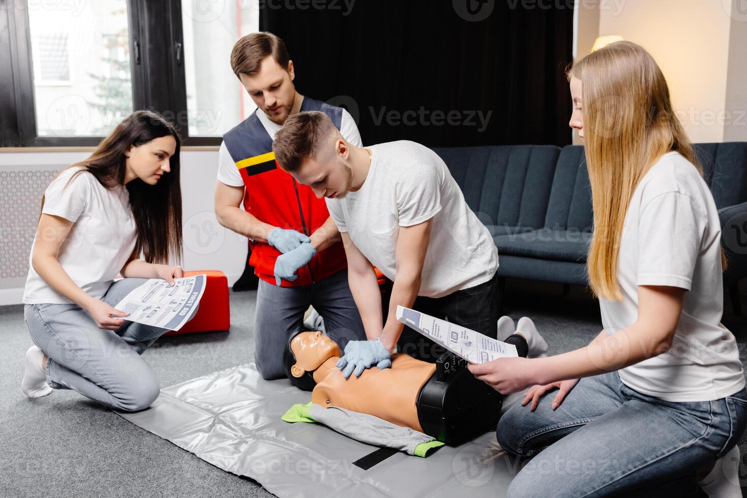 Young man instructor helping to make first aid heart compressions with dummy during the group training in room photo