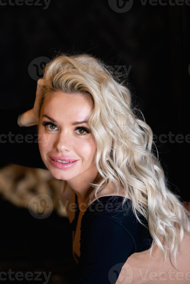 Beautiful blond woman with evening makeup, long waved hair, posing on black background.beauty portrait. photo