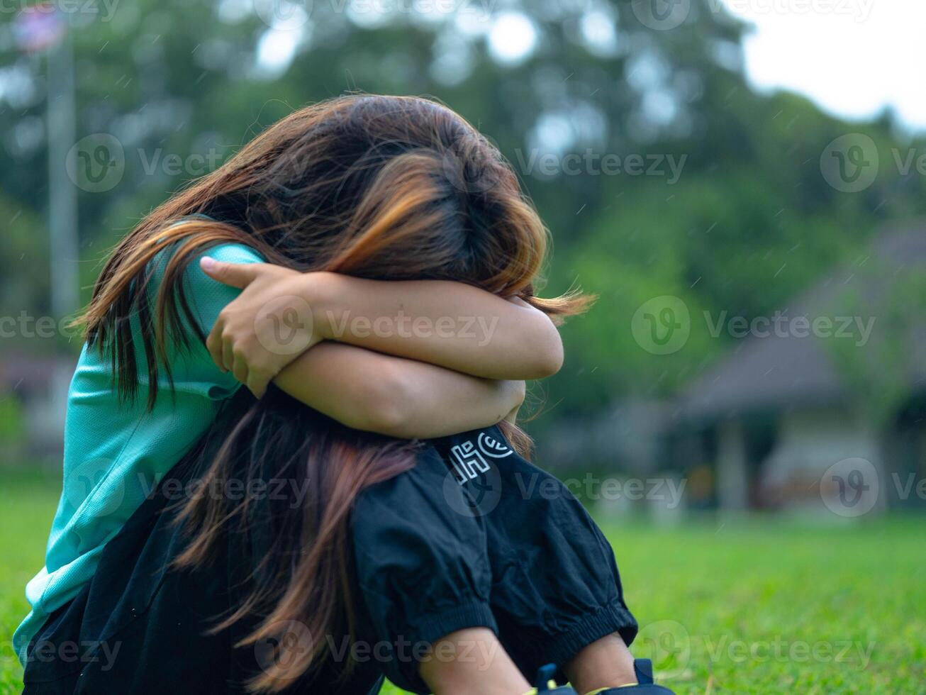 Unhappy sad little girl sitting alone hugging her knees in the park. photo