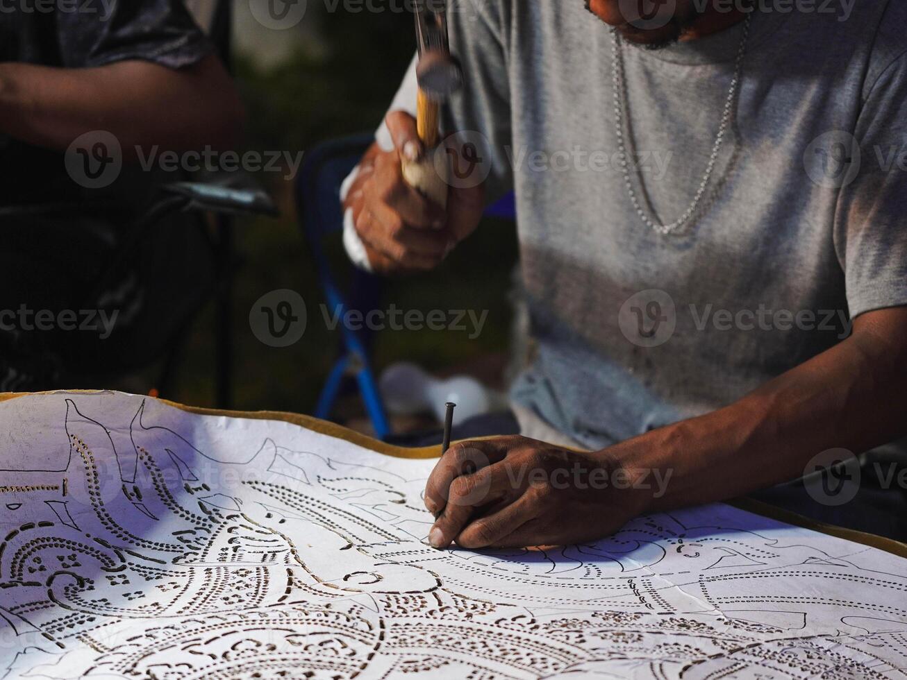 Close up hand of the craftsman is meticulously crafting traditional shadow puppets using tools and intricate techniques in a workshop. photo