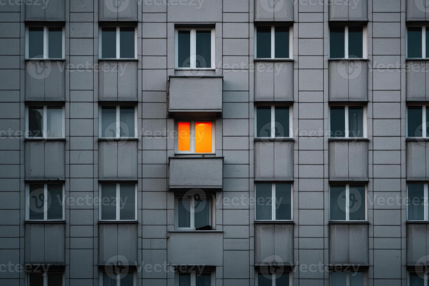 Lighted window contrasts against grey building facade during evening twilight photo