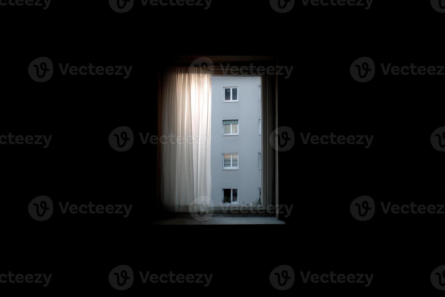 Light filters through a curtain, revealing a building across the street at dusk photo