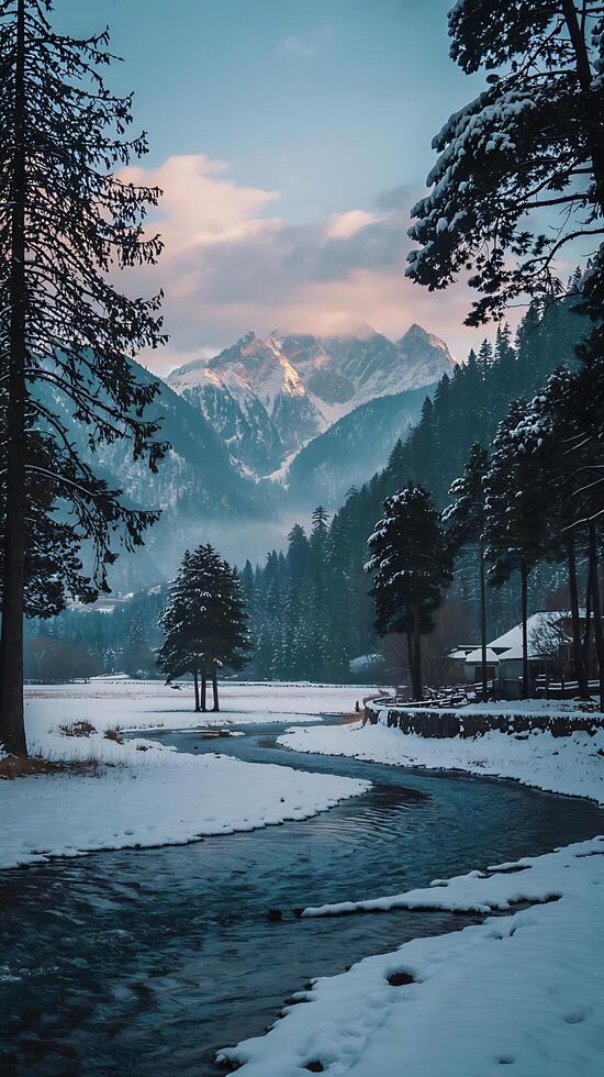 A river flows through a snowy field with trees and mountains in the background photo