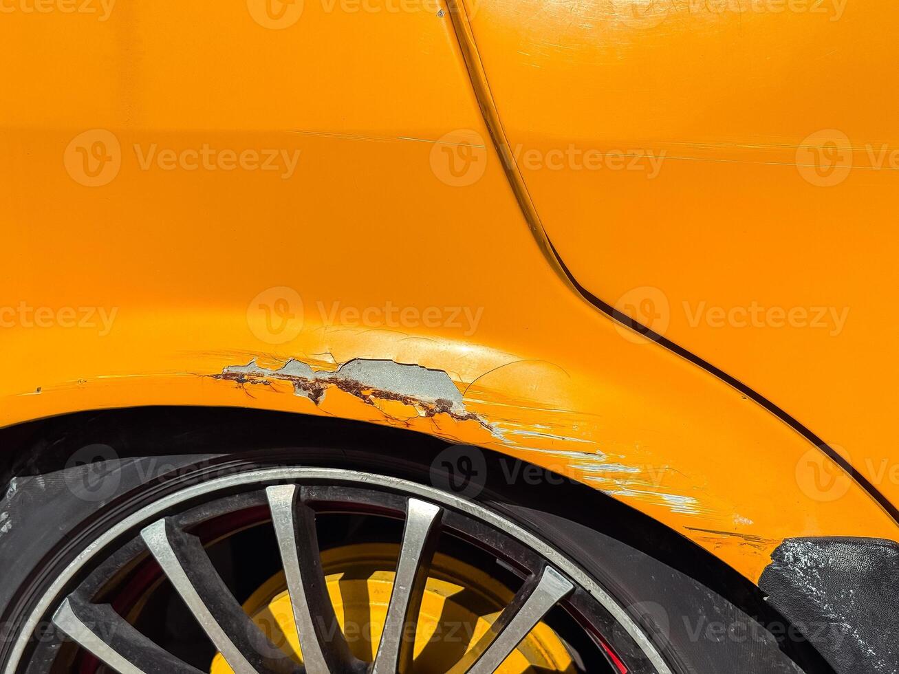 Retro Car damage on a bright orange vehicle with scratched paint and alloy wheels in sunlight photo