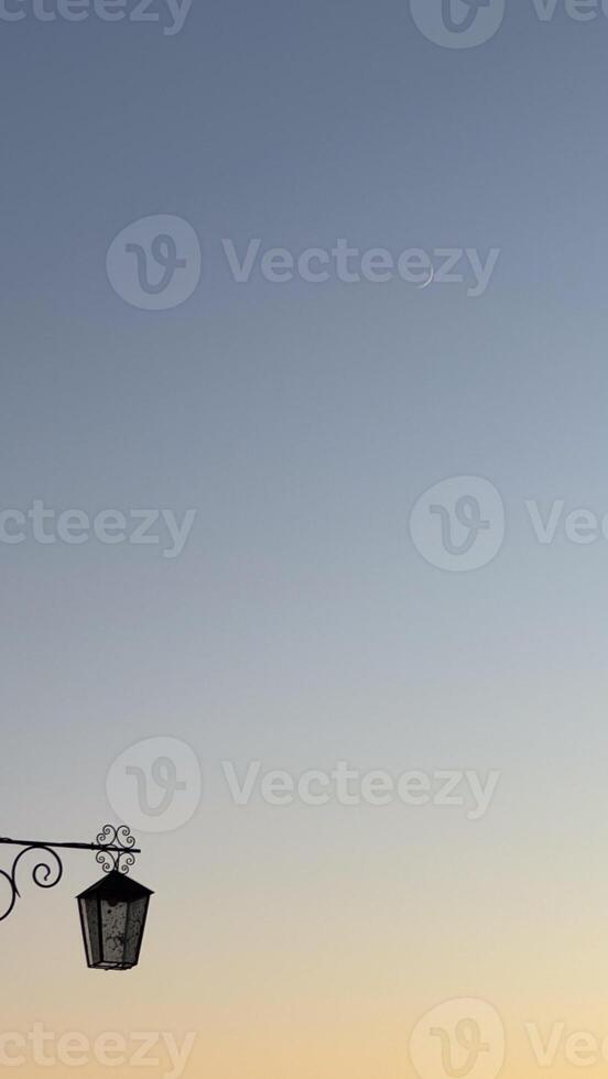 Serene evening sky with crescent moon above vintage lantern in minimalistic composition reflecting calm and simplicity of dusk time photo
