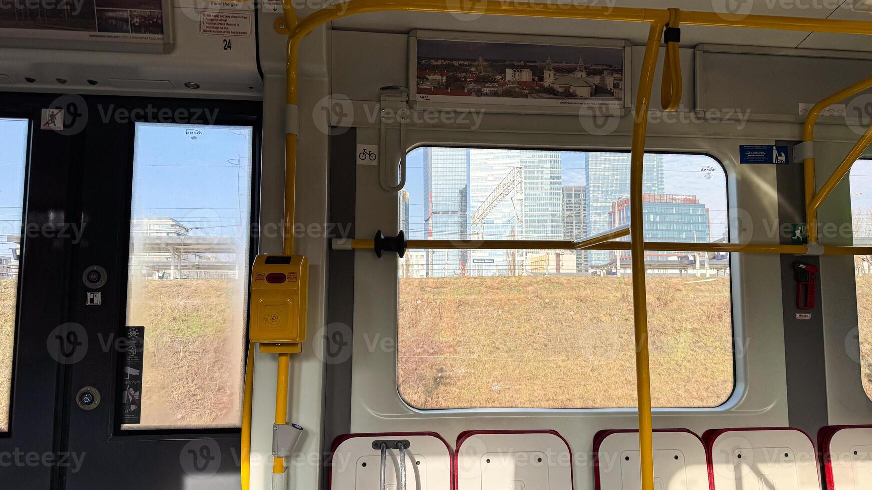 Interior view of modern city tram showing window reflections and urban landscape in daylight with yellow handrails and ticket validator photo