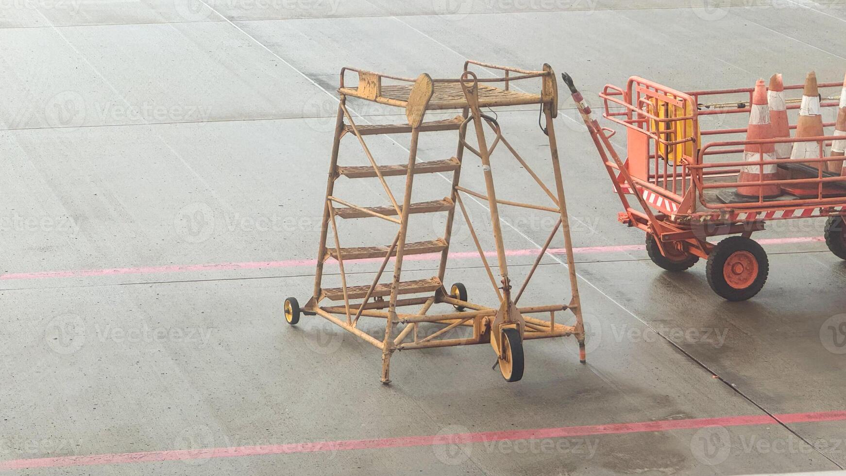 Vintage airport ground equipment, rustic wooden service steps and safety cones on concrete tarmac in overcast weather photo