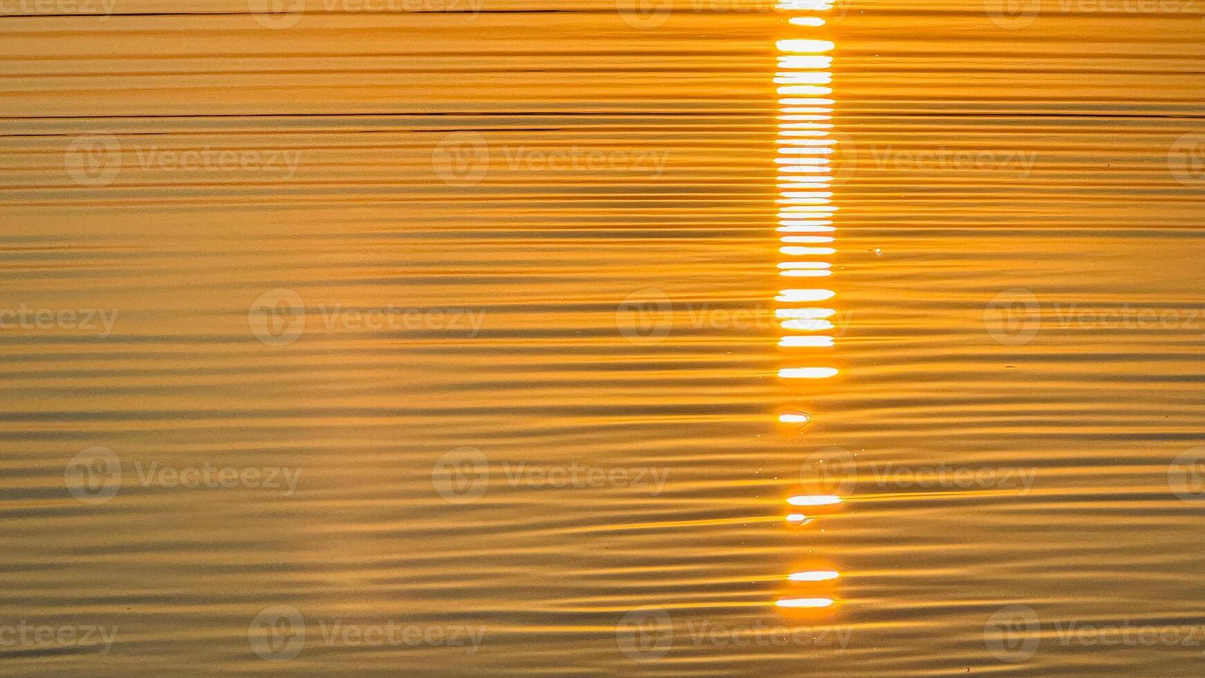 Golden sunset reflection on rippling water creating a warm tranquil ambiance with striking horizontal light patterns on the surface photo