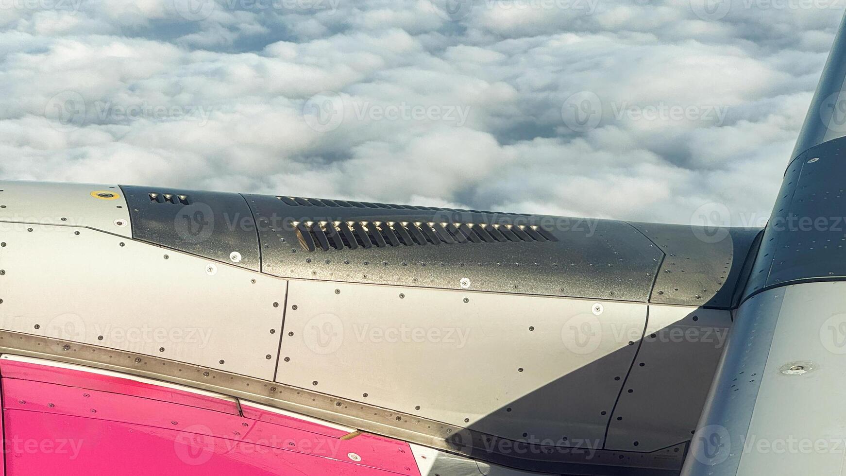 Striking view of an airplane wing and engine above a sea of white clouds captured during flight with sunlit metal surface photo
