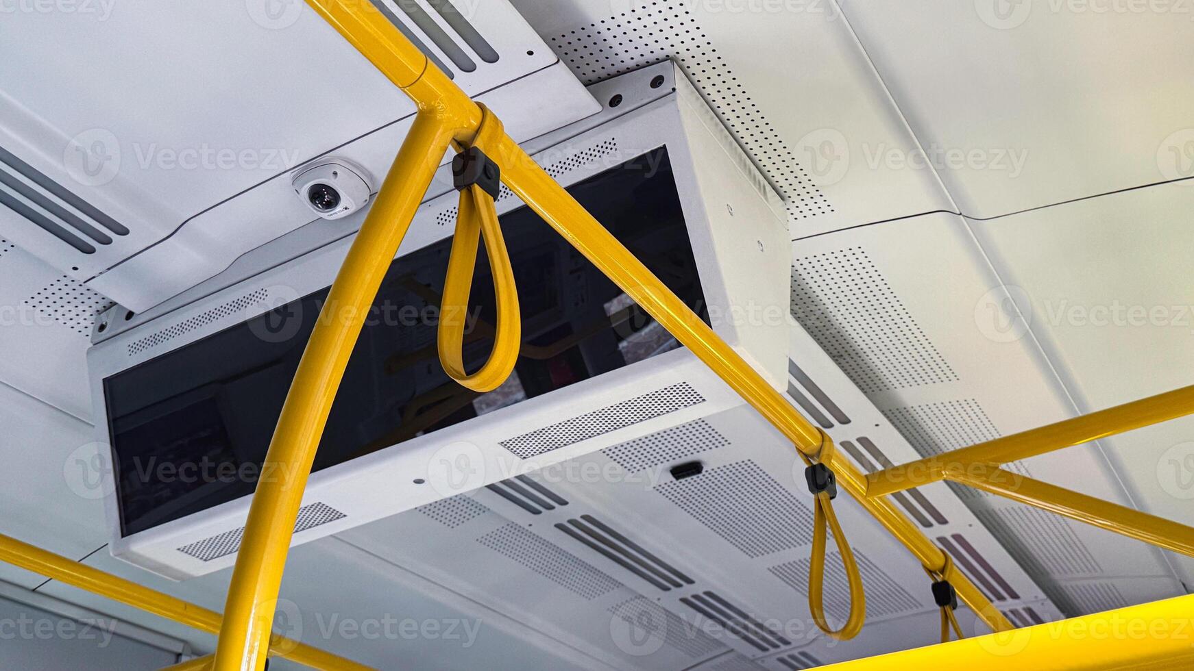 Yellow handrails and hanging loops inside modern public transportation vehicle with white ceiling and integrated surveillance camera photo