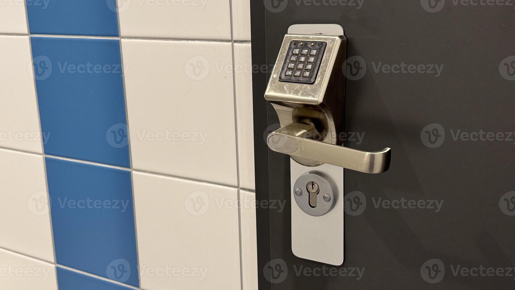 Modern electronic door lock with keypad on a dark door next to blue and white tiled wall showcasing advanced security technology photo
