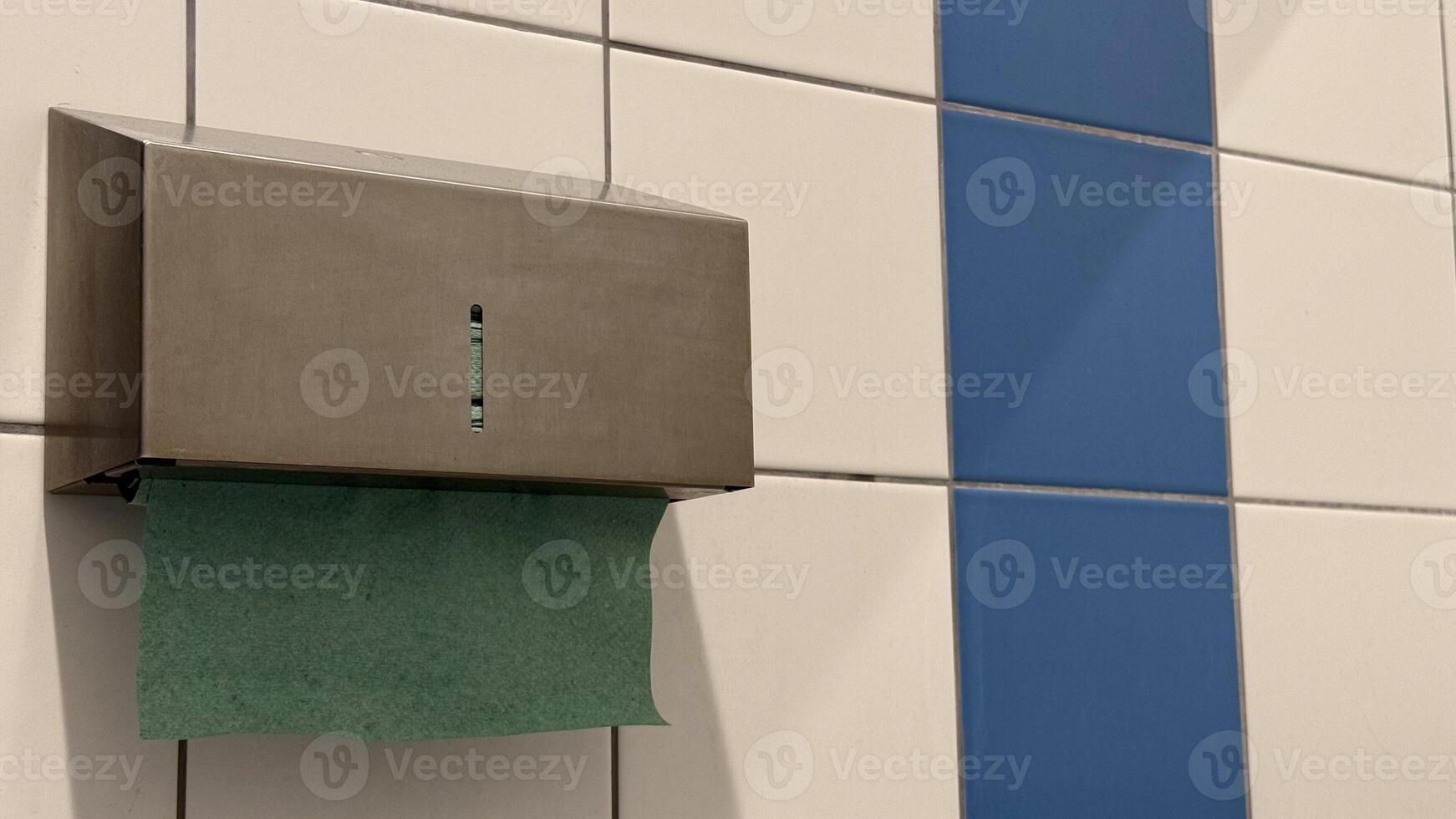 Stainless steel paper towel dispenser with green towel against white and blue tiled restroom wall captures minimalist design and utility photo
