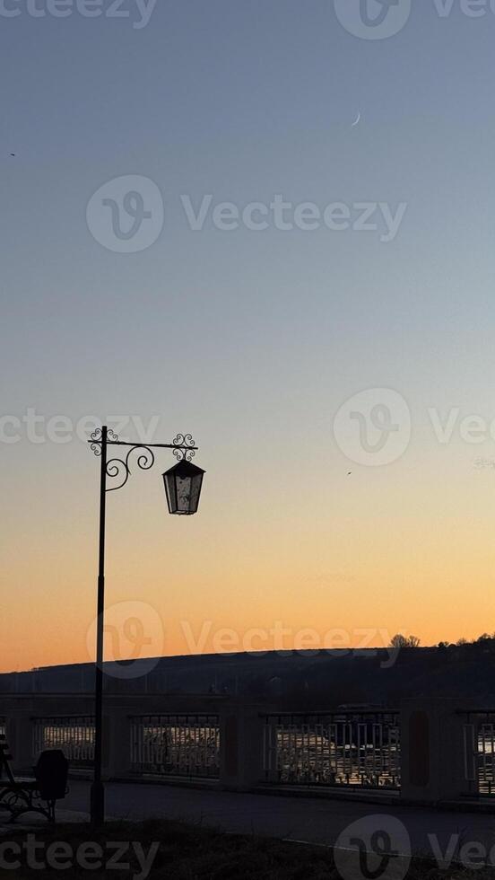 A serene dusk scene with an artistic vintage lamp post and a crescent moon against a peaceful sunset sky creating a tranquil atmosphere photo