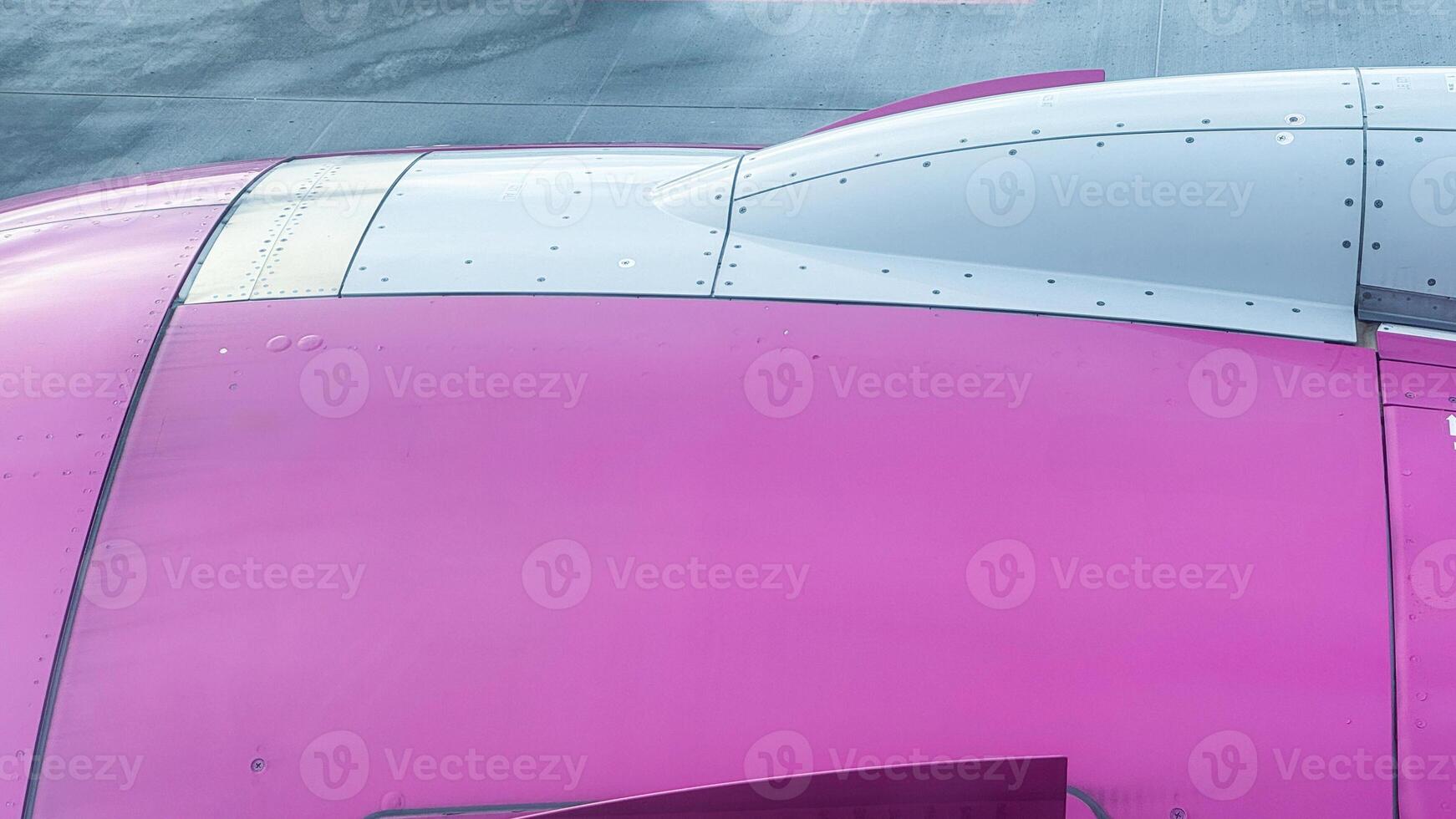 Close-up view of vibrant pink aircraft wing featuring metallic accents and smooth rivets at airport tarmac photo