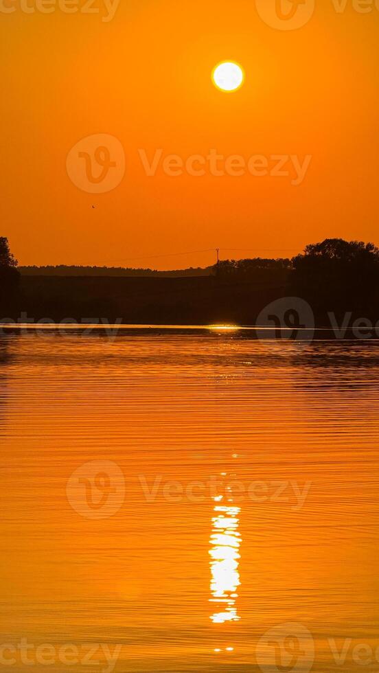 Glorious sunset over tranquil lake with golden reflections and scenic silhouettes of distant tree line creating a peaceful evening moment photo