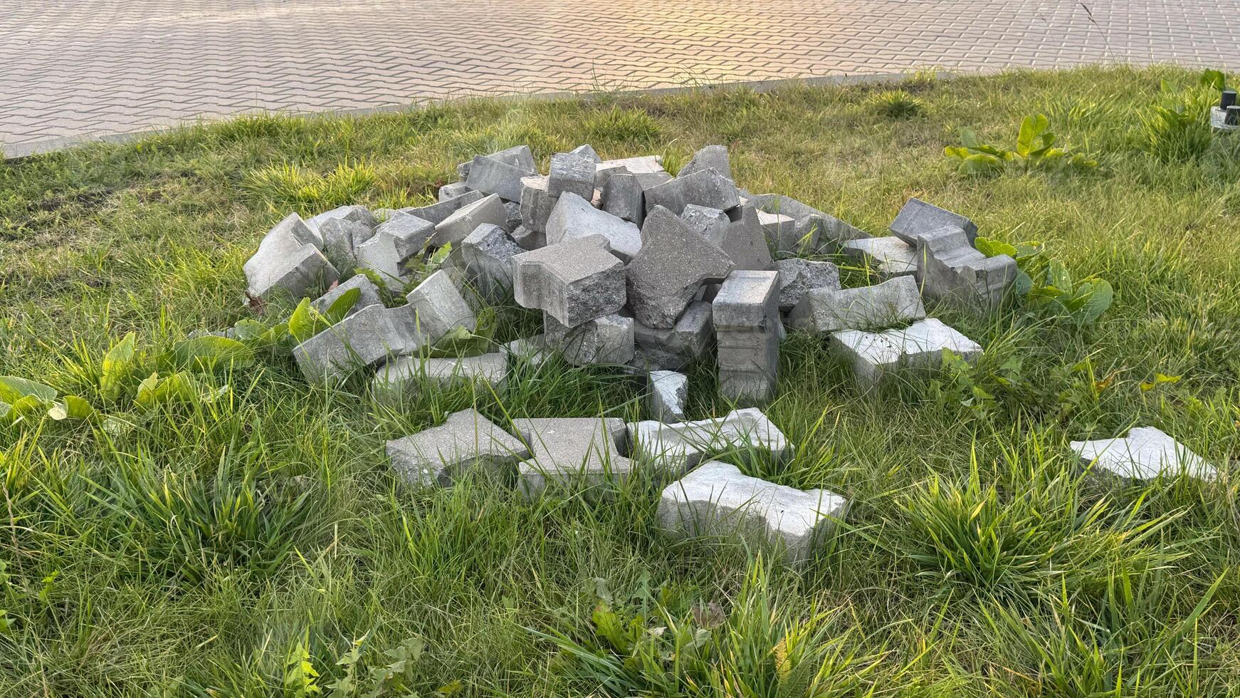Pile of gray concrete bricks on lush green grass next to paved road displaying an urban construction scene with natural elements photo